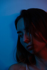 portrait photo of a woman in red neon light. Sad and lonely woman sitting leaning against the wall