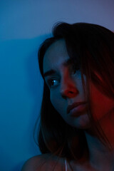 portrait photo of a woman in red neon light. Sad and lonely woman sitting leaning against the wall
