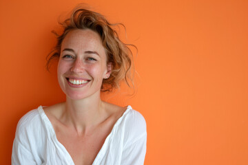 femme 30-35ans souriante portant un vêtement blanc sur fond uni orange, espace pour texte sur le coté