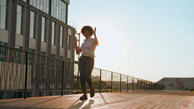 Female silhouette in sunshine city urban active playful happy girl African American business woman walking dancing moving to music rotate celebrate achievement success businesswoman dance go outdoors