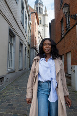 This image depicts a confident young African American woman walking down a cobblestone street in an...