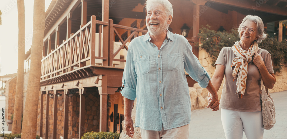 Sticker Portrait of one happy and cute senior holding hand of old pensioner wife walking and visiting new places together with the sunset at the background. Couple having fun in the park..