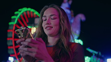 Closeup girl typing smartphone at illuminated ferris wheel. Happy model send