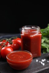 Delicious ketchup on black wooden table, closeup. Tomato sauce