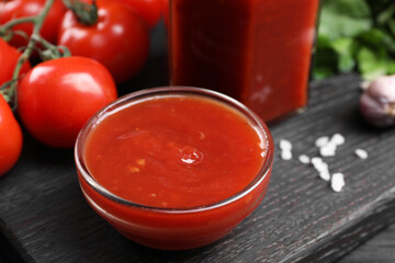 Delicious ketchup in bowl on black wooden table, closeup. Tomato sauce