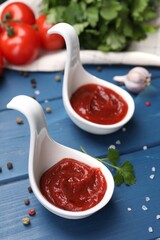 Organic ketchup in spoons and spices on blue wooden table, closeup. Tomato sauce