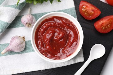 Organic ketchup in bowl, fresh tomatoes and garlic on table, flat lay. Tomato sauce