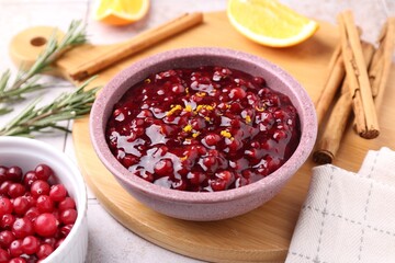 Tasty cranberry sauce in bowl and ingredients on white tiled table