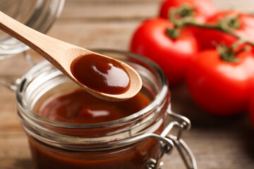 Taking tasty barbeque sauce from jar with spoon at table, closeup