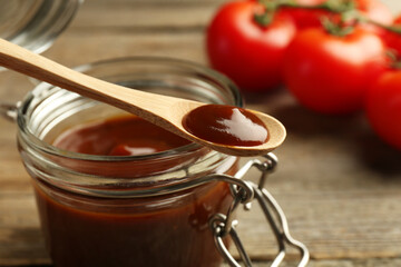 Tasty barbeque sauce in jar and spoon on table, closeup