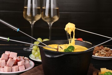 Dipping different products into fondue pot with melted cheese on table, closeup