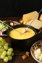 Fondue pot with melted cheese, forks and different products on wooden table