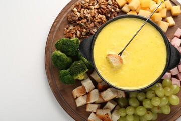 Fondue with tasty melted cheese, fork and different products on white table, top view