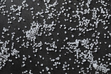 Scattered white natural salt on black table, top view