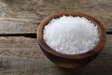 Organic salt in bowl on wooden table, closeup. Space for text