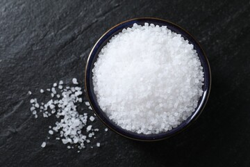 Organic white salt in bowl on black table, top view