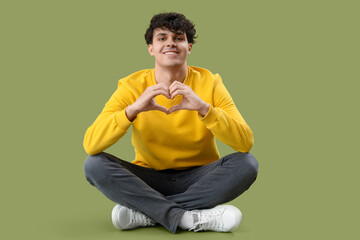 Handsome young man making heart with his hands on green background