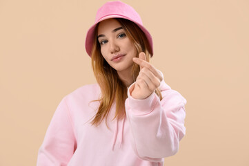 Young woman making heart with her fingers on beige background