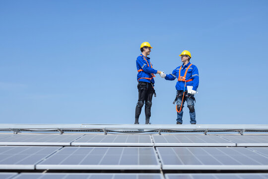 Engineers with handshake gesture on solar panels against blue sky
