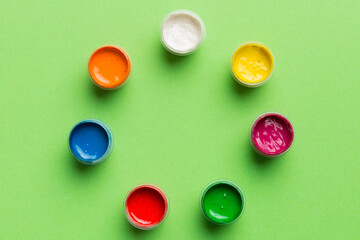 jars with gouache of different colors on Colored background. hobby painting. Top view with empty...