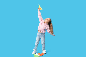 Cute little girl with paper planes on blue background