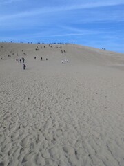 Fototapeta na wymiar Upward slope of Tottori sand dune with footprints in the foreground, travellers walking up to the top in far away background, wint a blue sky with white clouds