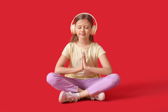 Little girl in headphones meditating on red background