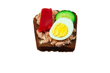 sandwich with fish, red pepper, cucumber and boiled egg. a piece of black bread with fish and vegetables on a white background	