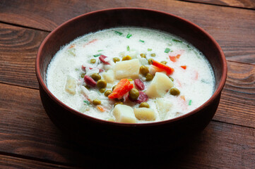 cheese soup in a clay plate on a wooden background. soup with young vegetables on a brown table. home cooking concept	