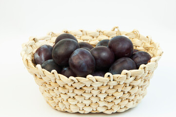 round blue plums in a basket on a white background. ripe sweet plums on a light texture