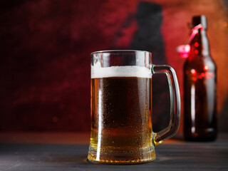 Light cold beer mug with drops of water on a wooden table. A bottle of beer