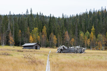 Old wooden hay barns next to Riisin rietas trail wooden path in autumnal Riisitunturi National Park, Northern Finland