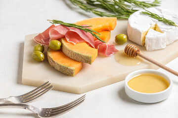 Board with tasty melon, prosciutto, cheese and honey on light background, closeup