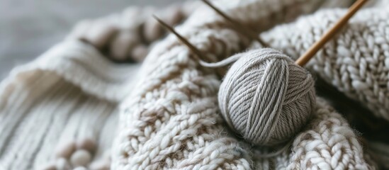 This photo features a white background with a ball of grey yarn and a pair of knitting needles. The yarn is neatly wound into a ball, ready to be used for knitting projects. The knitting needles are - Powered by Adobe