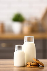 Bottles of fresh milk with sweet cookies on wooden table in kitchen