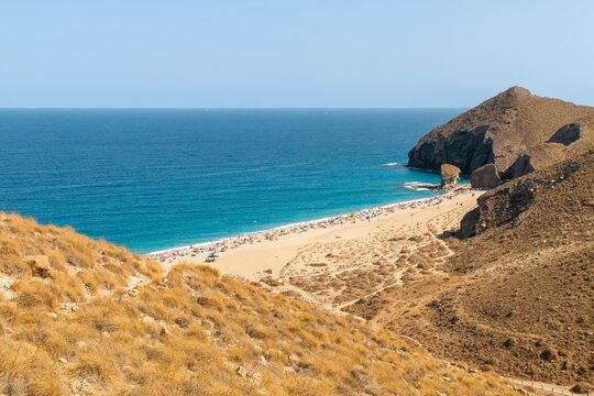 Bañistas tomando el sol en la playa de Los Muertos, Carboneras, Almería, España. Vista cenital de la playa a orillas del mar Mediterráneo con sus aguas turquesas un soleado día de verano.