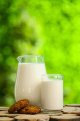 Glass and jug of fresh milk with sweet cookies on wooden table outdoors