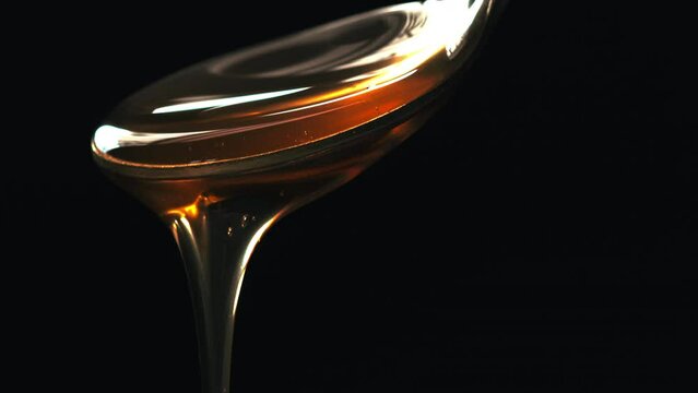 Cuchara vertiendo miel con fondo negro. L&iacute;quido marr&oacute;n viscoso que cae suavemente. Textura liquida. Macro 60fps 4k
