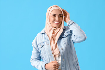 Stylish Muslim woman in denim jacket on blue background