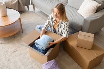 Young woman putting folded sweater in box at home