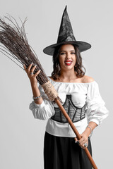 Young witch with broom on light background