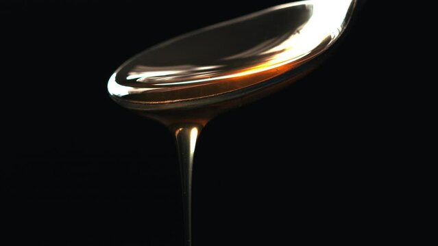 Cuchara vertiendo miel con fondo negro. Líquido marrón viscoso que cae suavemente. Textura. Macro 60fps