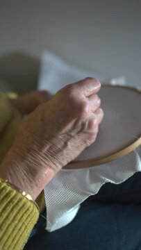 Detail of finger pointing cross-stitch drawing, hands of seventy-year-old woman, older. Squares, stitches and colours of pattern as a model for design.