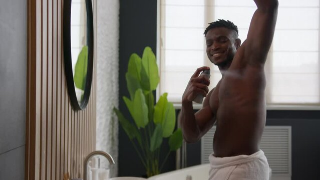 Smiling shirtless African American man applying deodorant antiperspirant in armpit get ready looking in bathroom mirror male everyday hygiene hyperhidrosis treatment sweat protection daily skincare
