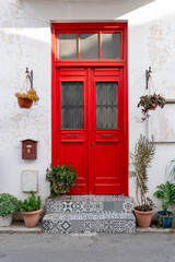 Fototapeta na wymiar Bright red front door. Authentic street of the Cypriot city. Cute entrance to the house decorated with flowers. Travel photo. Greek culture. Colourful mood