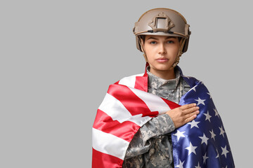 Young female soldier in uniform with flag of USA on grey background