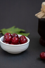 Fresh ripe cherry berry in a white bowl on dark background. Preserved berries, homemade jam. Copy space, vertical photo