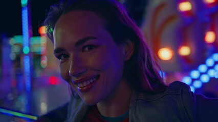 Smiling girl posing neon amusement park closeup. Happy teen enjoying weekend