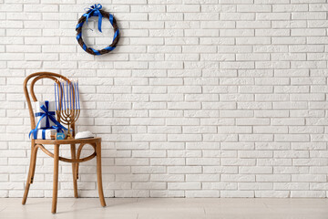 Wooden chair with menorah, gift boxes and dreidel near white brick wall. Hanukkah celebration