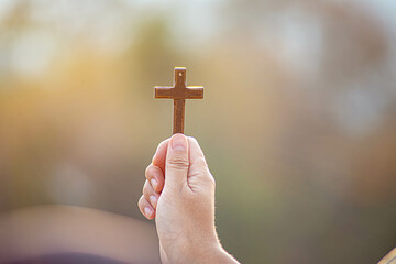 Human hand holding cross with light sunset background. christian concept
